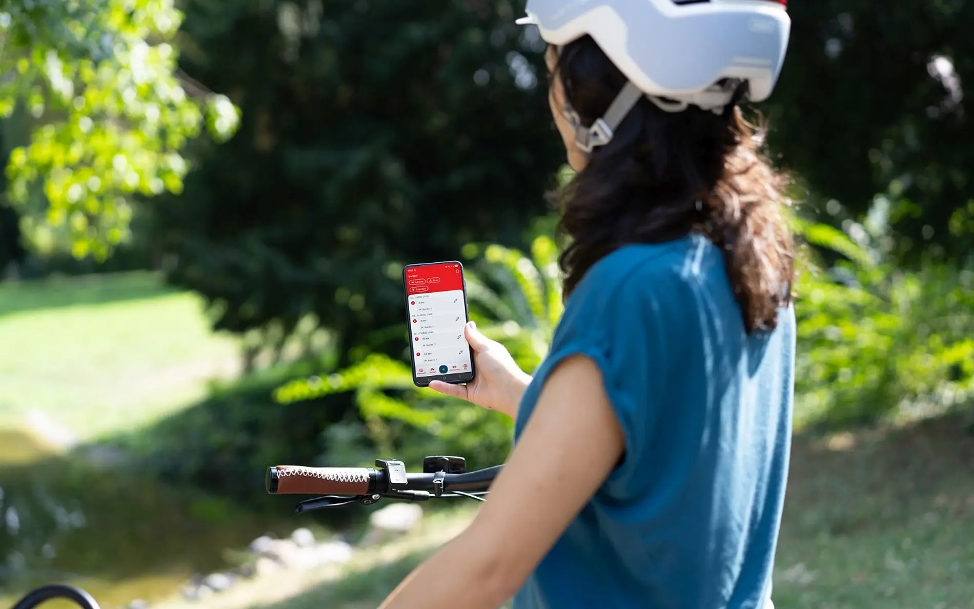 Frau mit Fahrradhelm von hinten. Sie hält ein Handy mit der Österreich radelt App