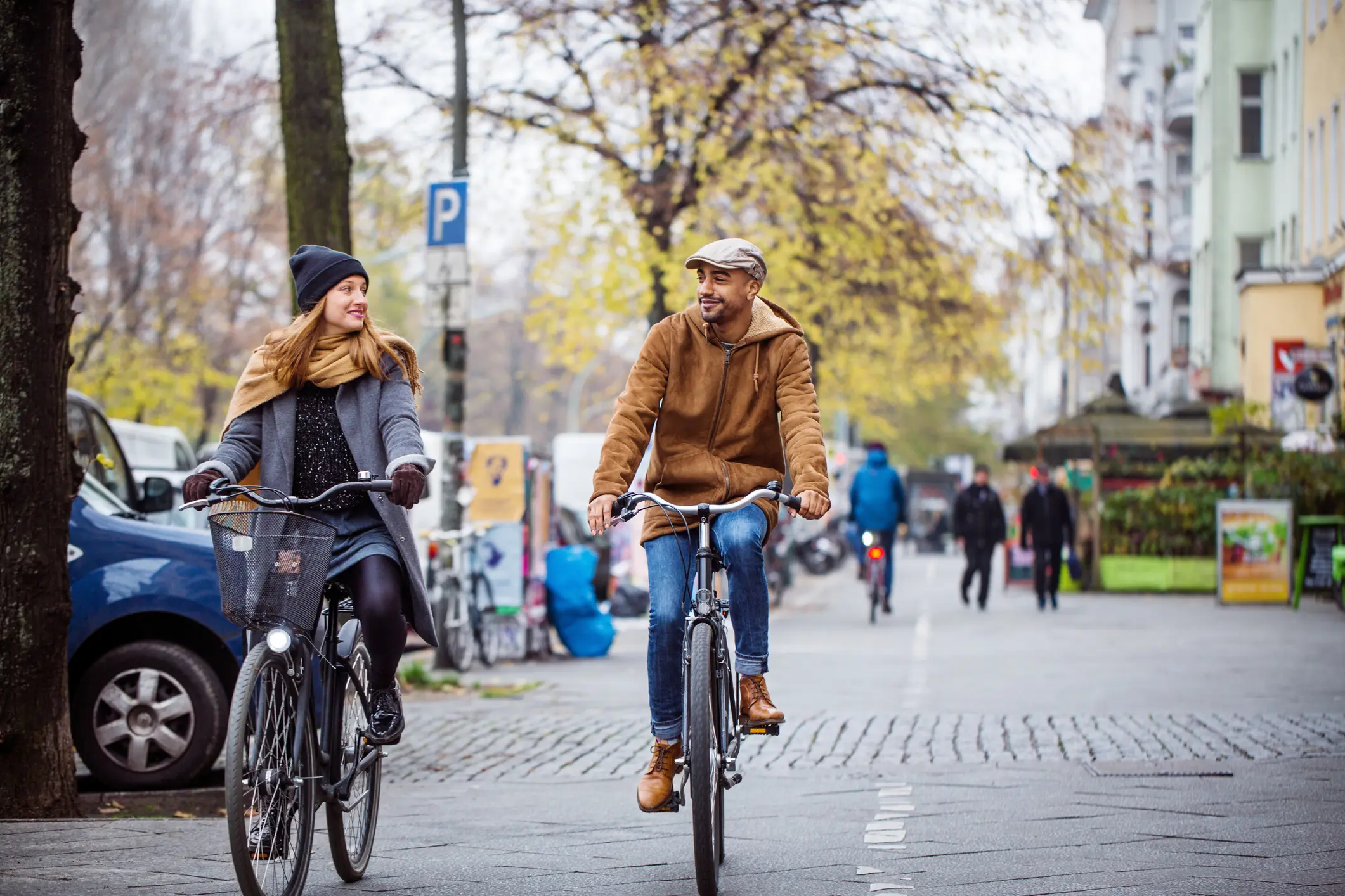 Zwei Personen radeln nebeneinander auf einer breiten Straße. Sie tragen Winterkleidung.