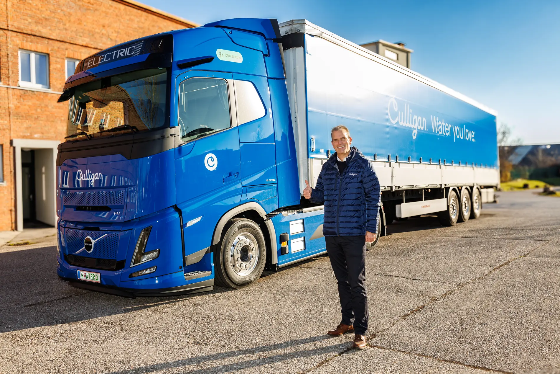 Lächelnder Mann steht vor elektrisch betriebenem, blauen Lastkraftwagen.
