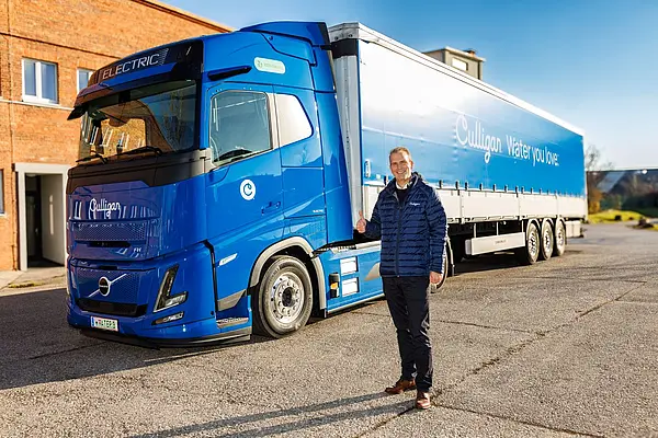Lächelnder Mann steht vor elektrisch betriebenem, blauen Lastkraftwagen.