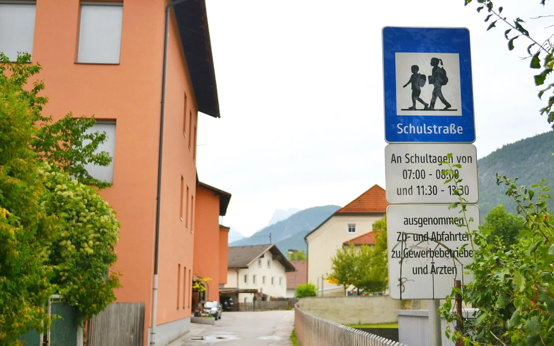 Schild Schulstraße mit genauen Zeitangaben, dahinter Schulgebäude und Straße