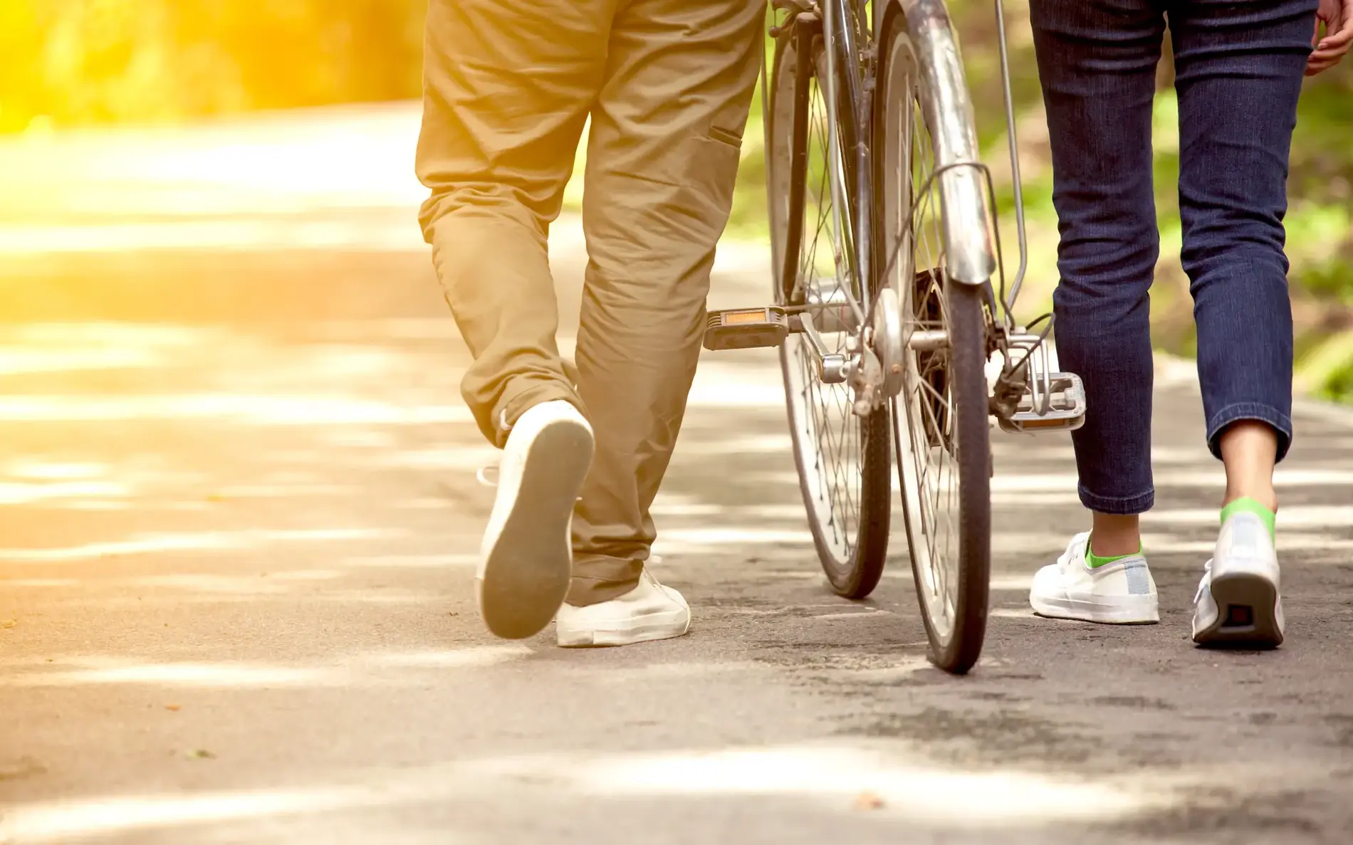 2 Personen gehen am Weg entlang, eine davon schiebt ein Fahrrad