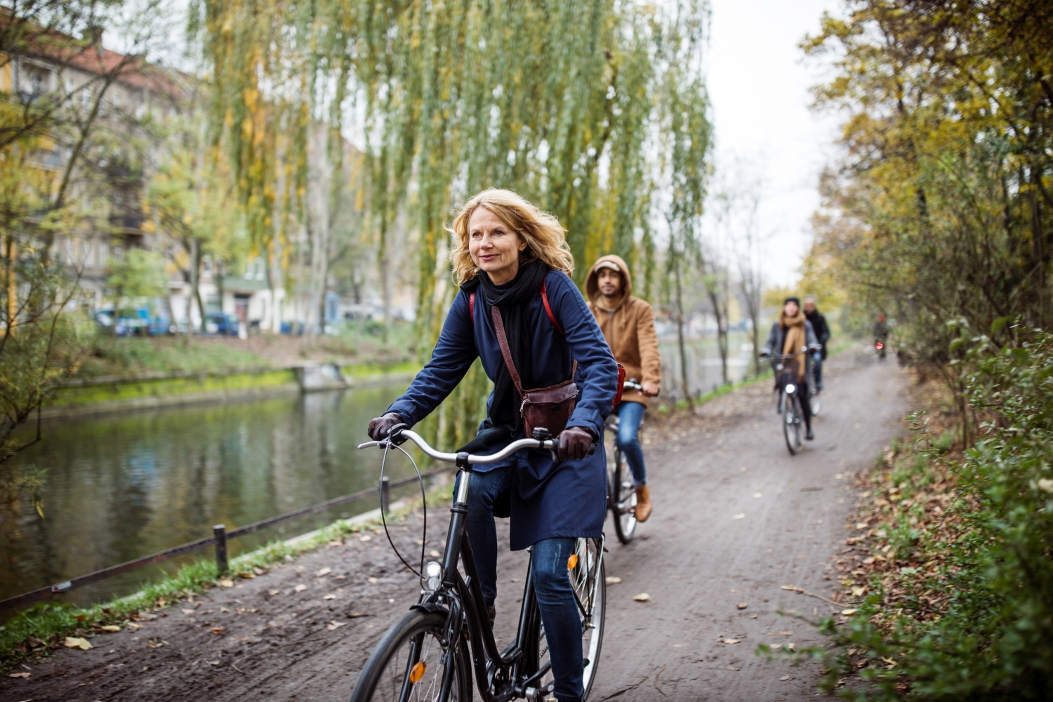 ältere Frau mit schulterlangen hellen Haaren radelt entlang eines Flussbeets am Radweg, dahinter zwei weitere Personen