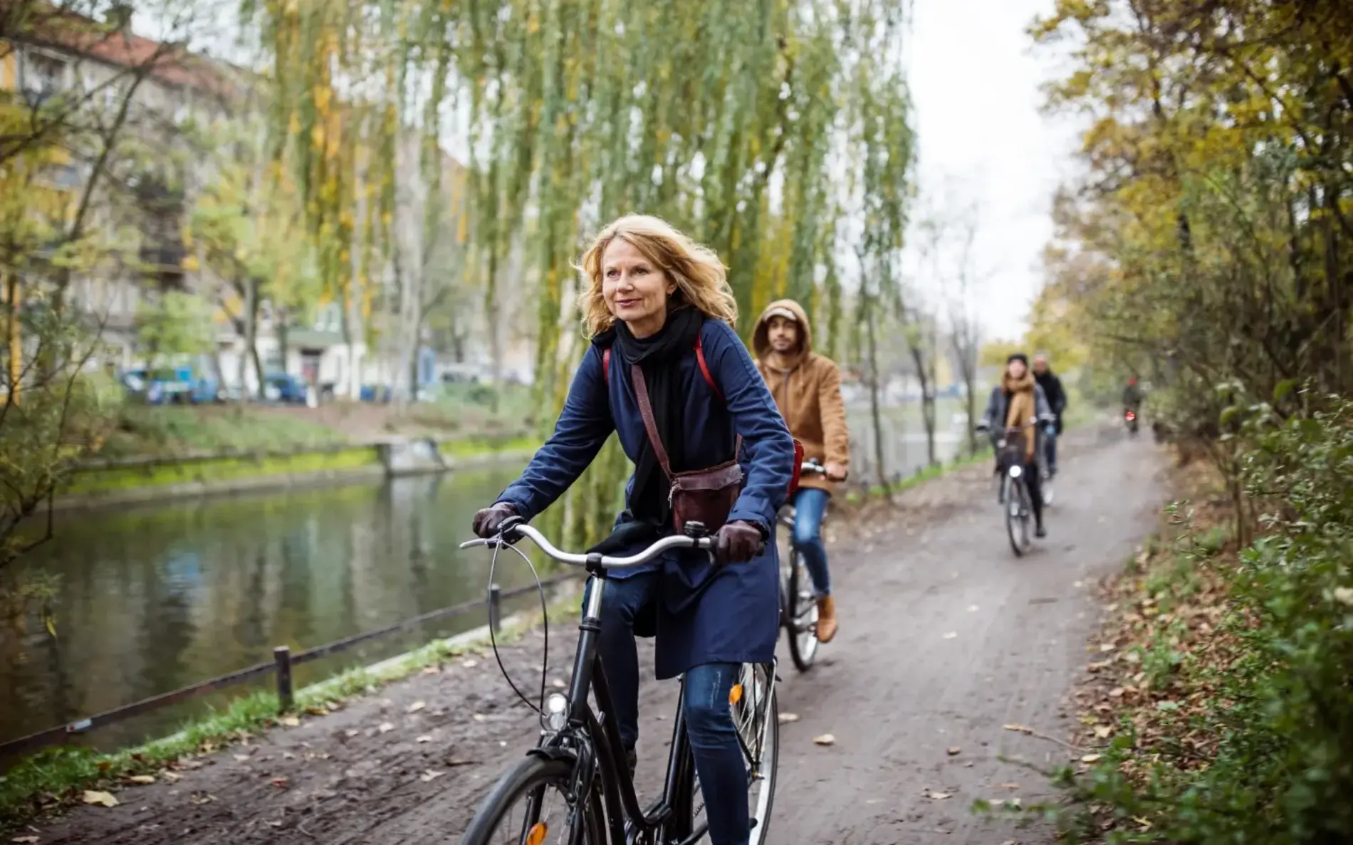 ältere Frau mit schulterlangen hellen Haaren radelt entlang eines Flussbeets am Radweg, dahinter zwei weitere Personen