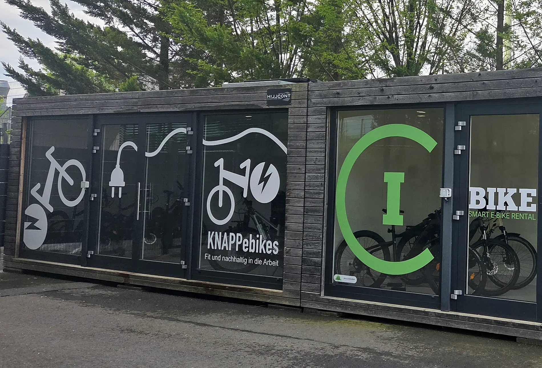 Zwei geschlossene Fahrradgaragen in der Größe von Containern, Glasfront mit Türen, Aufschrift Bike-Box, drinnen Fahrräder, steht im Freien