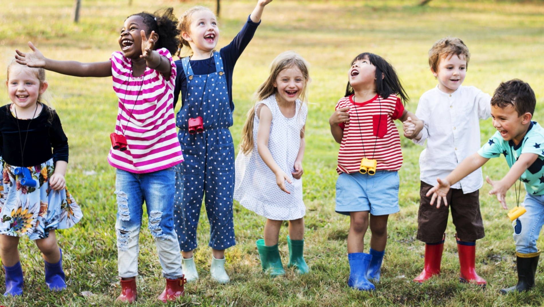 Kindergartenkinder in Gummistiefeln auf einer Wiese springend