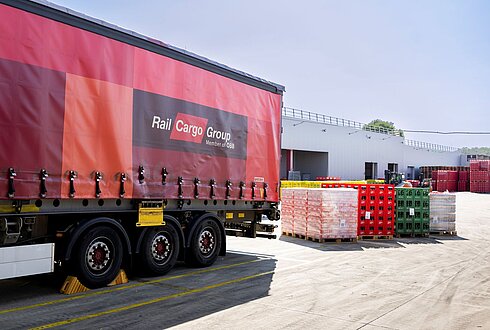 Hinteres Ende von Lastkraftwagen mit Aufschrift Rail Cargo Group, daneben große Getränkegebinde am Boden