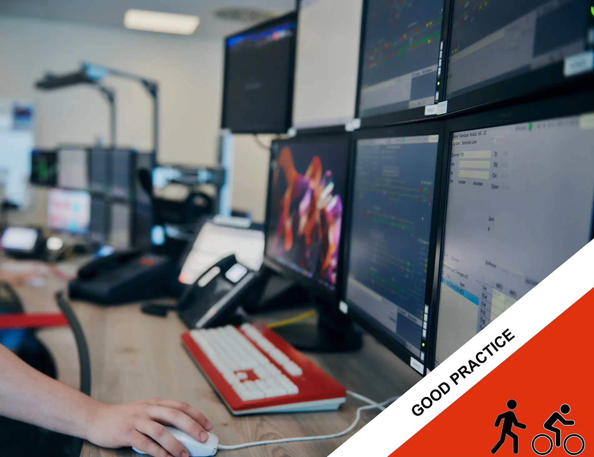 A workstation with multiple computer monitors displaying software applications and data dashboards is set up on a desk, with a person using a mouse in the foreground.