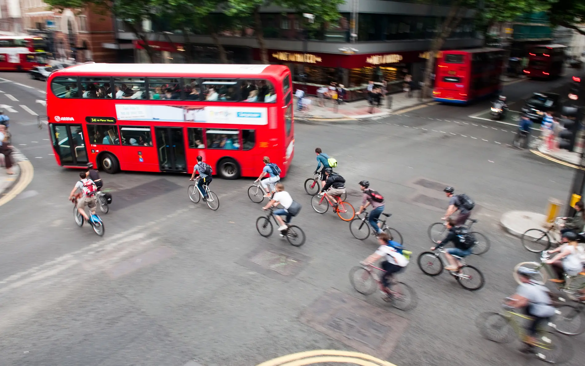 Szene einer Rush Hour in London: Roter Doppeldeckerbus, viele Radfahrende an der Kreuzung