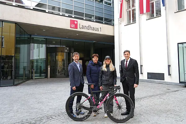 vor Gebäude vom Land Tirol, vier Personen stehen nebeneinander, von links nach rechts: Mann mit Sacko, Frau in Mantel, Frau mit Kappe und Jacke, Herr in Anzug und Krawatte, davor ein neues Fahrrad, Blick in Richtung Kamera