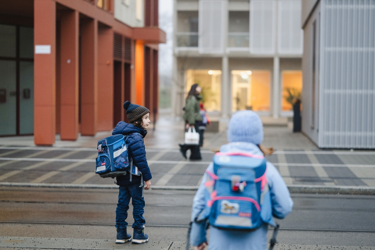 Zwei Schulkinder vor einer modernen Schule. Sie sind in Winterkleidung eingepackt