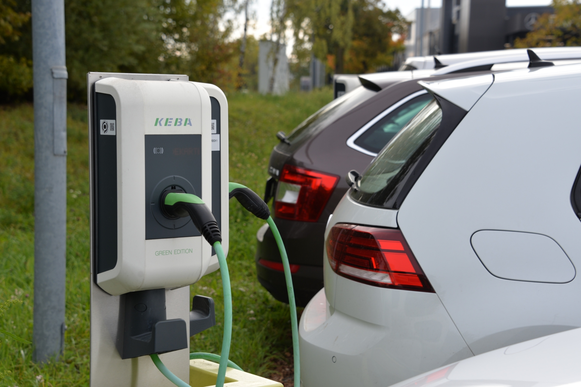 Mehrere Pkw werden auf einem Parkplatz über elektrische Ladestationen aufgeladen