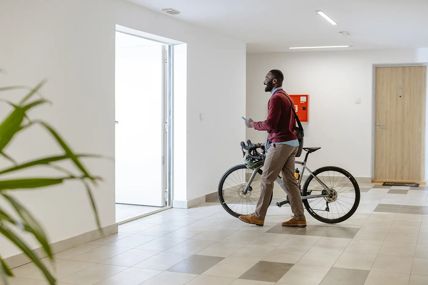 Mann schiebt Fahrrad aus dem großen Haus-Eingang und hält in der anderen Hand ein Handy