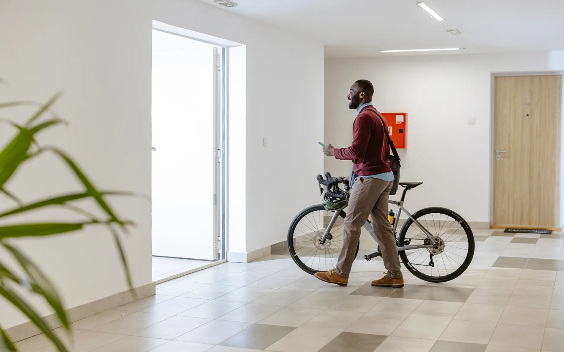 Mann schiebt Fahrrad aus dem großen Haus-Eingang und hält in der anderen Hand ein Handy