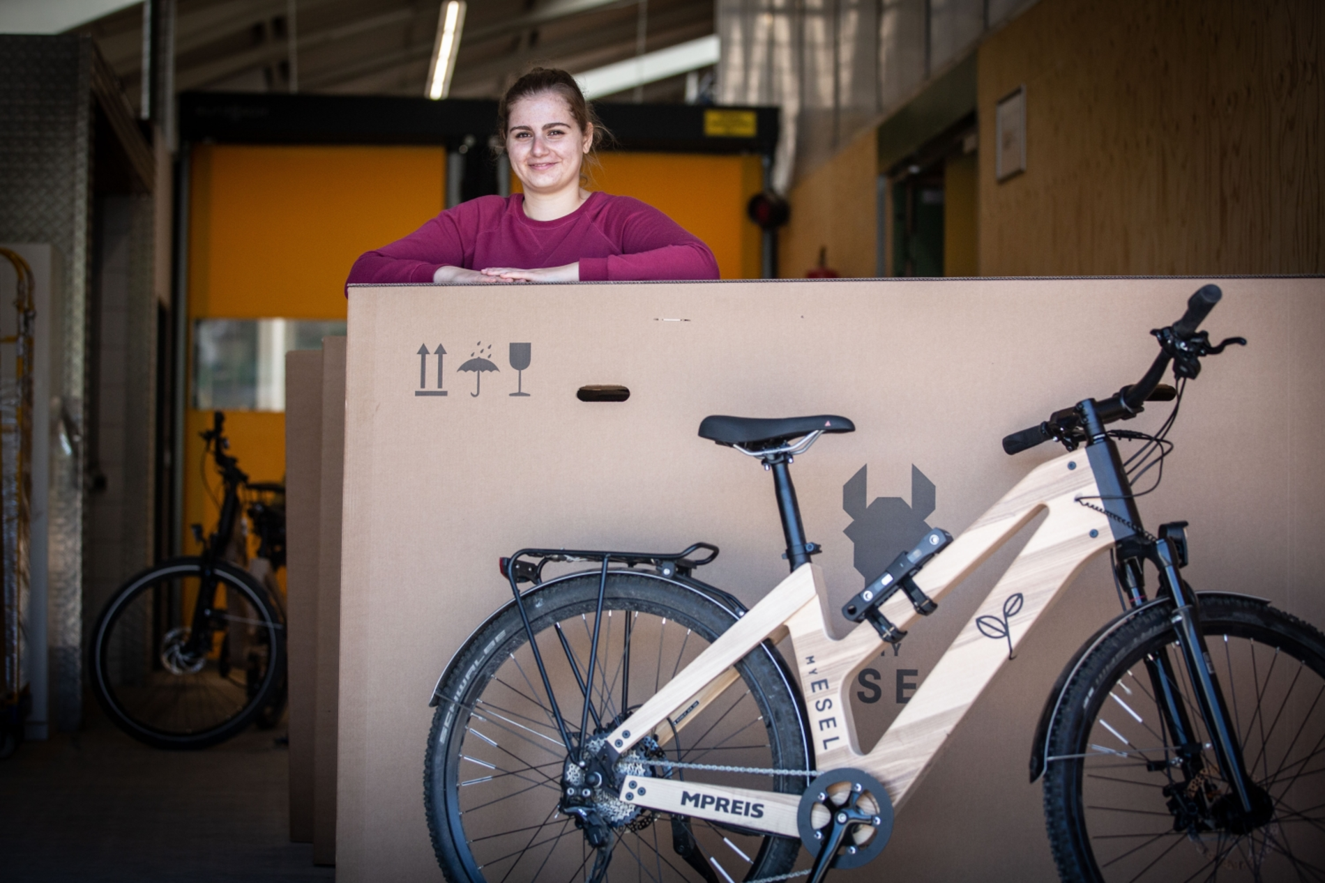 Fahrrad mit einem Holzrahmen, dahinter steht eine Frau