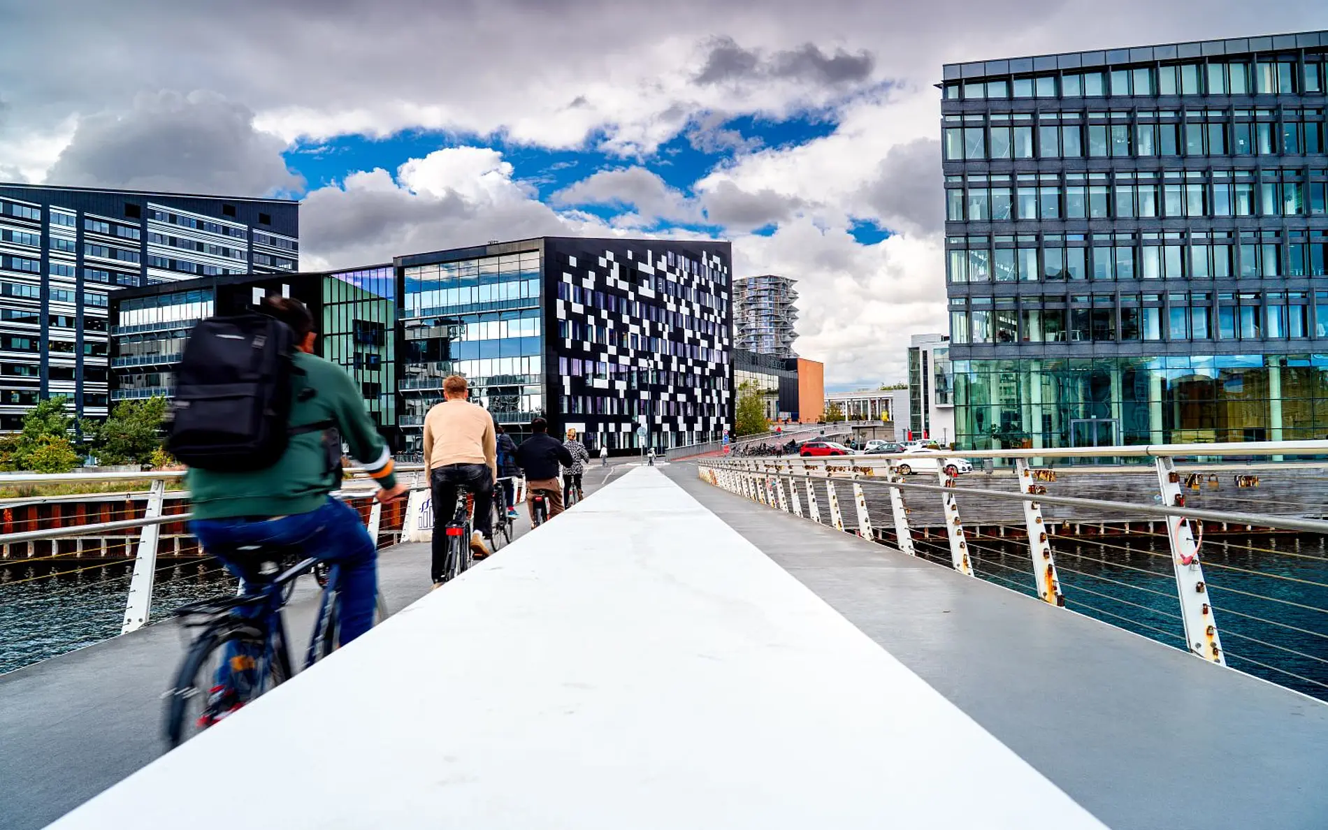 Radfahrer:innen über eine moderne Brücke in Kopenhagen, im Hintergrund moderne Glasgebäude