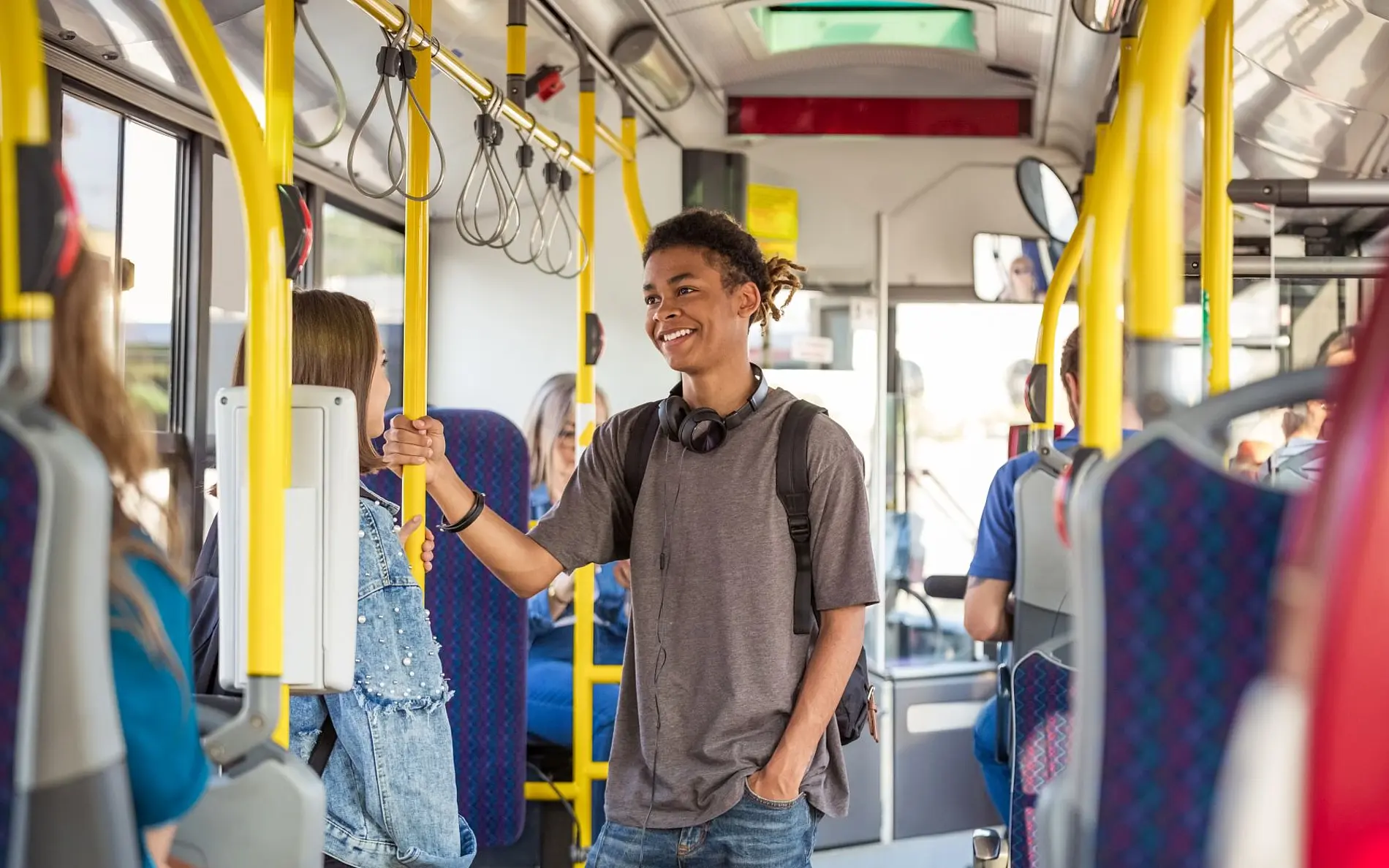 Jugendlicher im Innenraum des Busses. Hält sich an der Stange fest und redet mit einem Mädchen