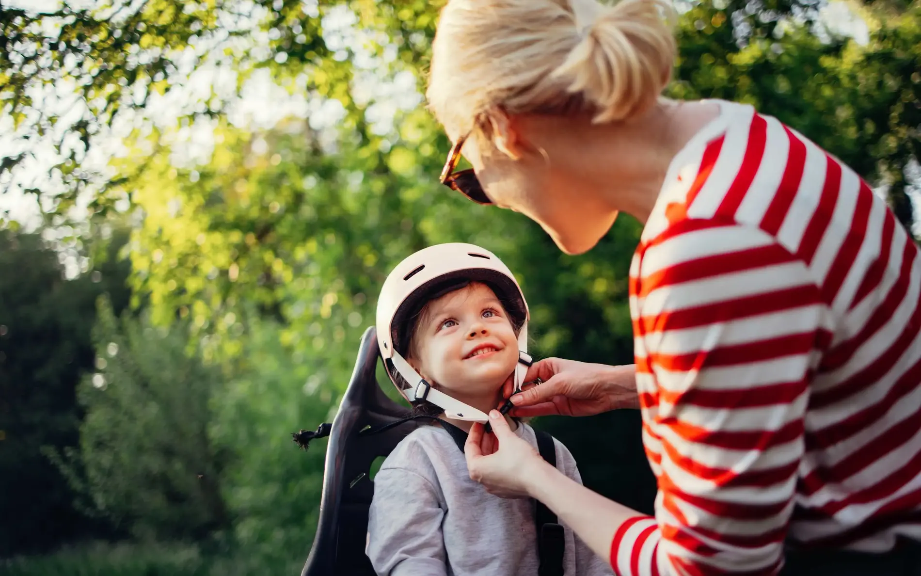 Eine Mutter macht ihrem Kind den Helm zu am Fahrradsitz