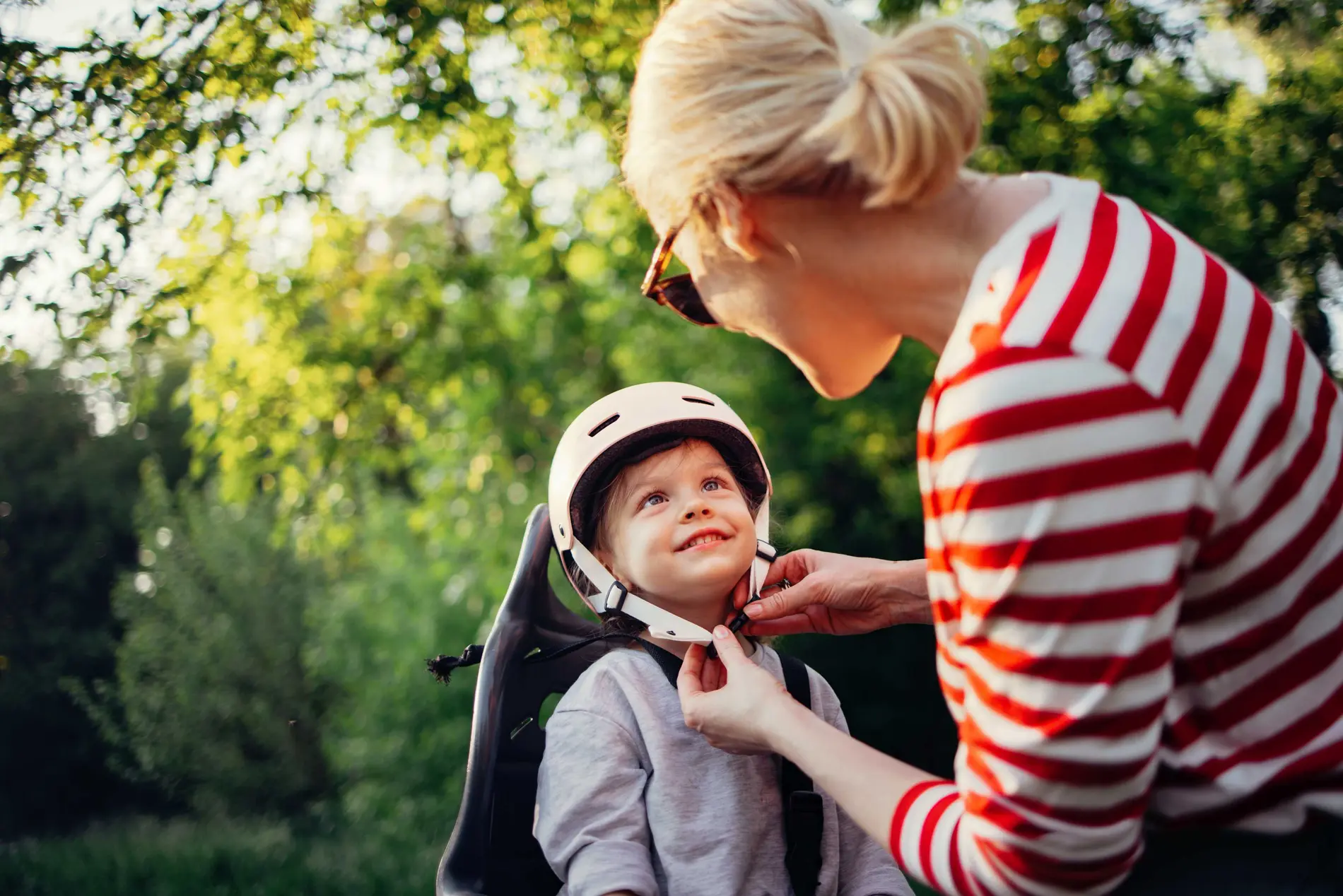 Radfahren mit Kindersitz Tipps Eine Mutter macht ihrem Kind den Helm zu am Fahrradsitz