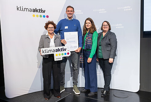 4 Personen mit Urkunde und klimaaktiv Schild schauen in die Kamera