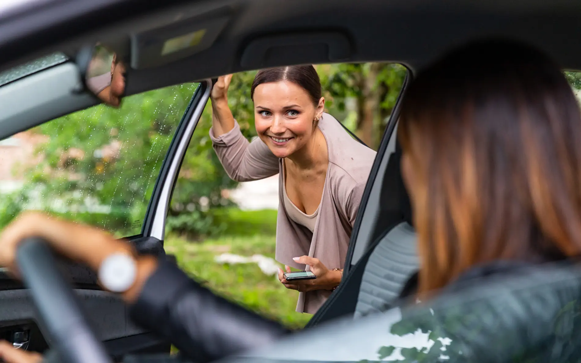 Eine Frau steigt zu einer anderen Frau ins Auto und lächelt dabei.
