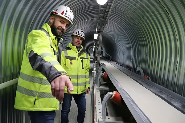 Zwei Mitarbeitende des Bad Ischler Trockenmörtelwerks stehen in gelben Warnwesten neben der neu errichtetetn Förderbandanlage.