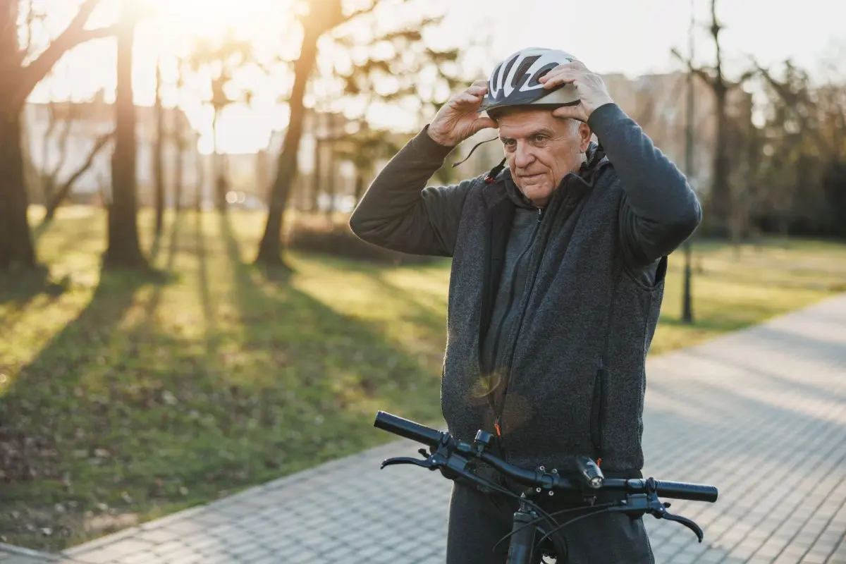 Ein älterer Mann mit steht mit dem Fahrrad auf einem Weg und setzt sich gerade den Fahrradhelm auf