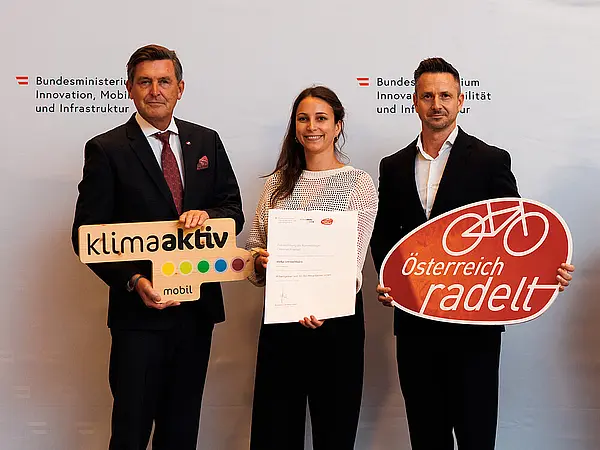 Bundesminister Peter Hanke und zwei weitere Personen stehen nebeneinander, halten klimaaktiv mobil Logo, Österreich radelt Logo und Urkunde in den Händen