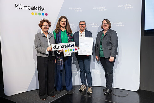 4 Personen mit Urkunde und klimaaktiv Schild schauen in die Kamera