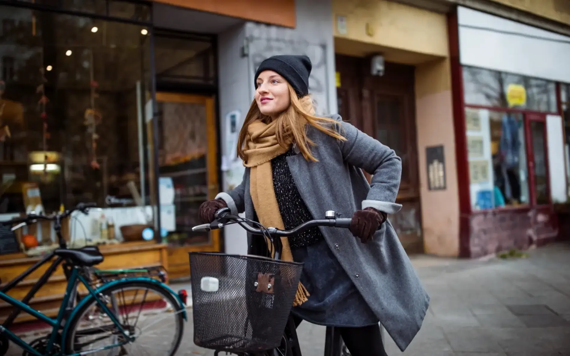 Eine Frau mit Wintermütze, Jacke und Schal steigt auf das fahrende Rad, im Hintergrund eine Hausreihe