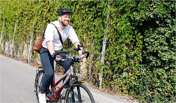 Mann in weißem Hemd und brauner Umhängetasche fährt am Fahrrad in die Arbeit