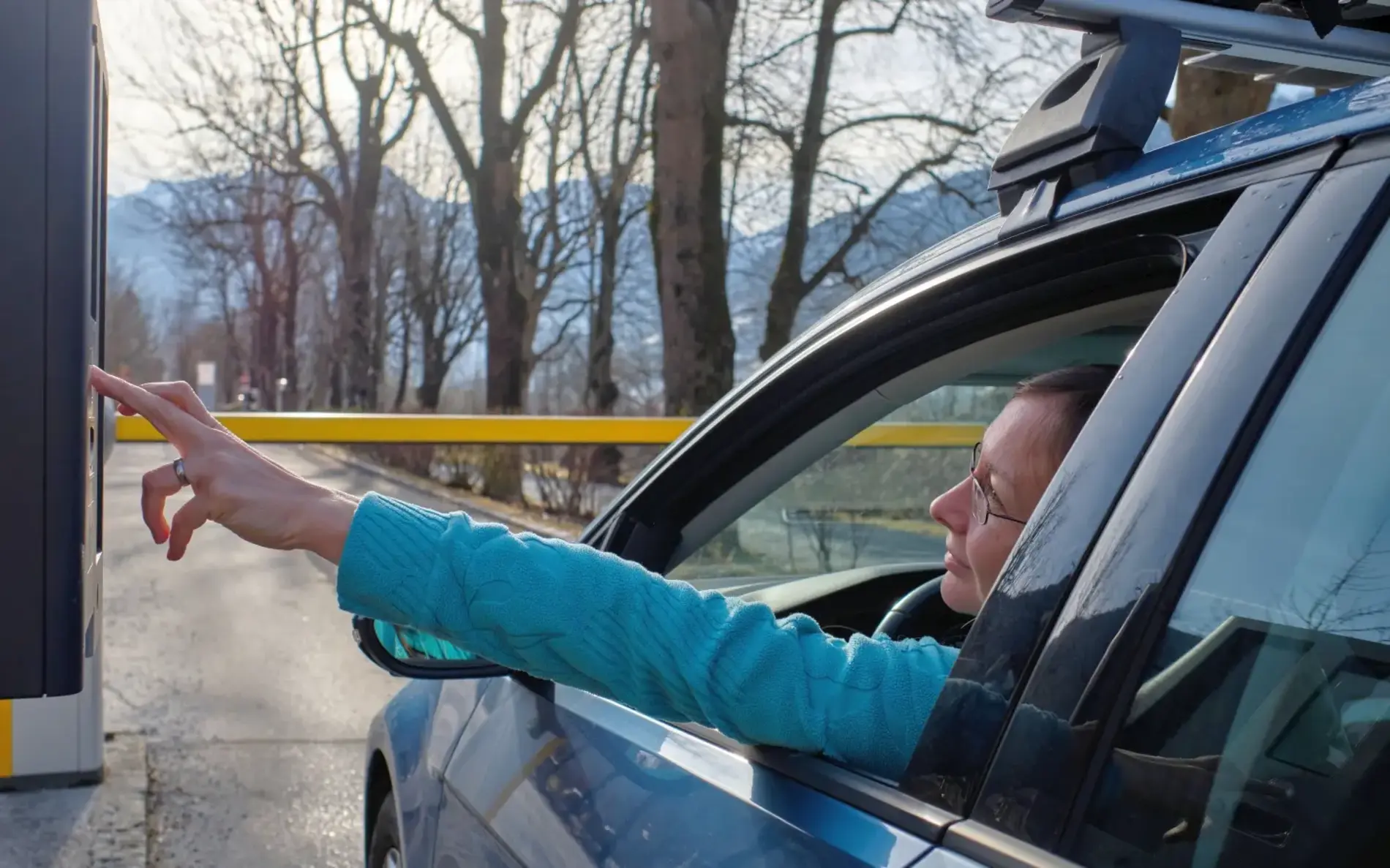 Frau steht mit Auto vor Schranke und drückt einen Parkschein raus