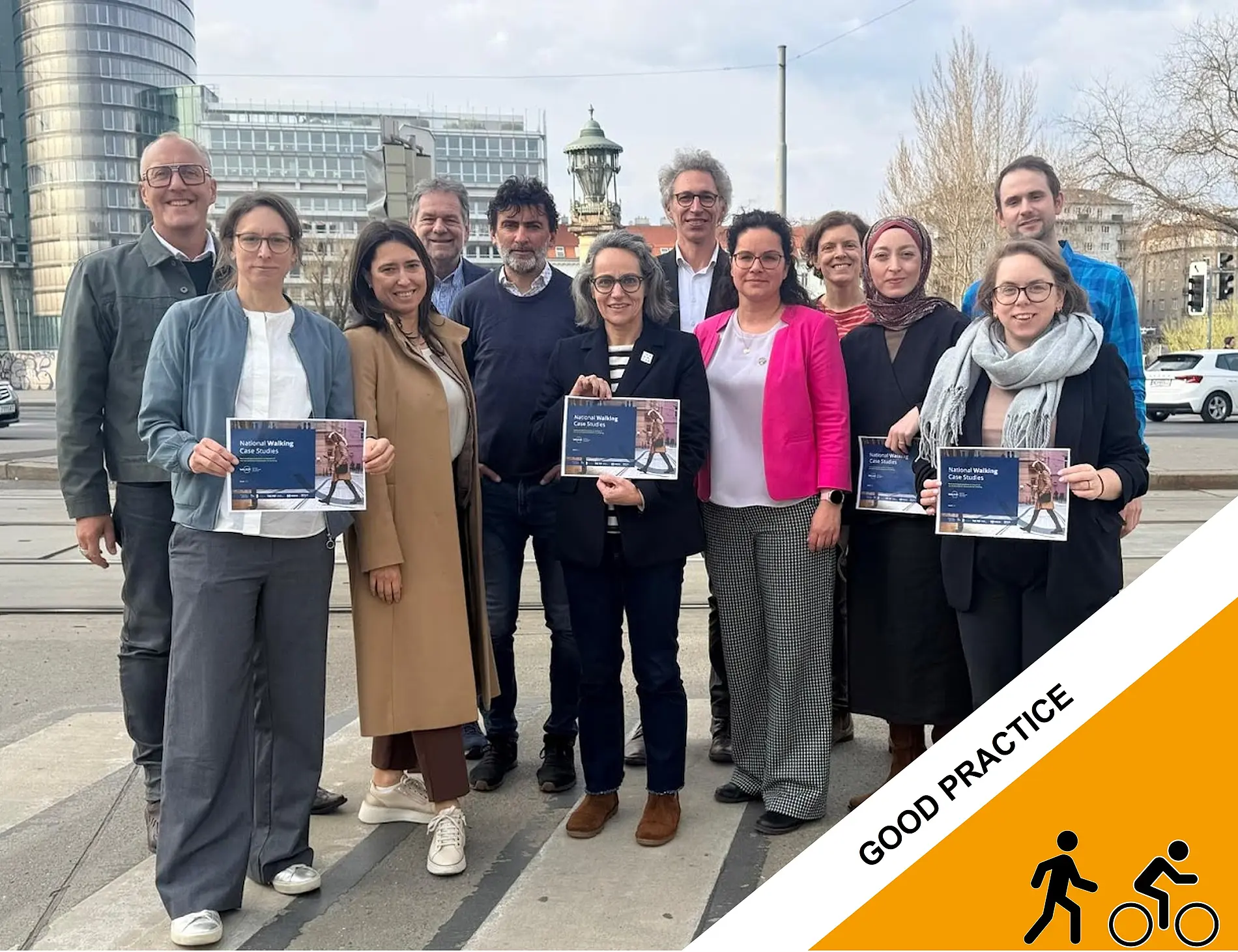 A group of participants at THE PEP project stand outdoors in an urban setting holding project flyers, with modern buildings and a tower visible in the background.