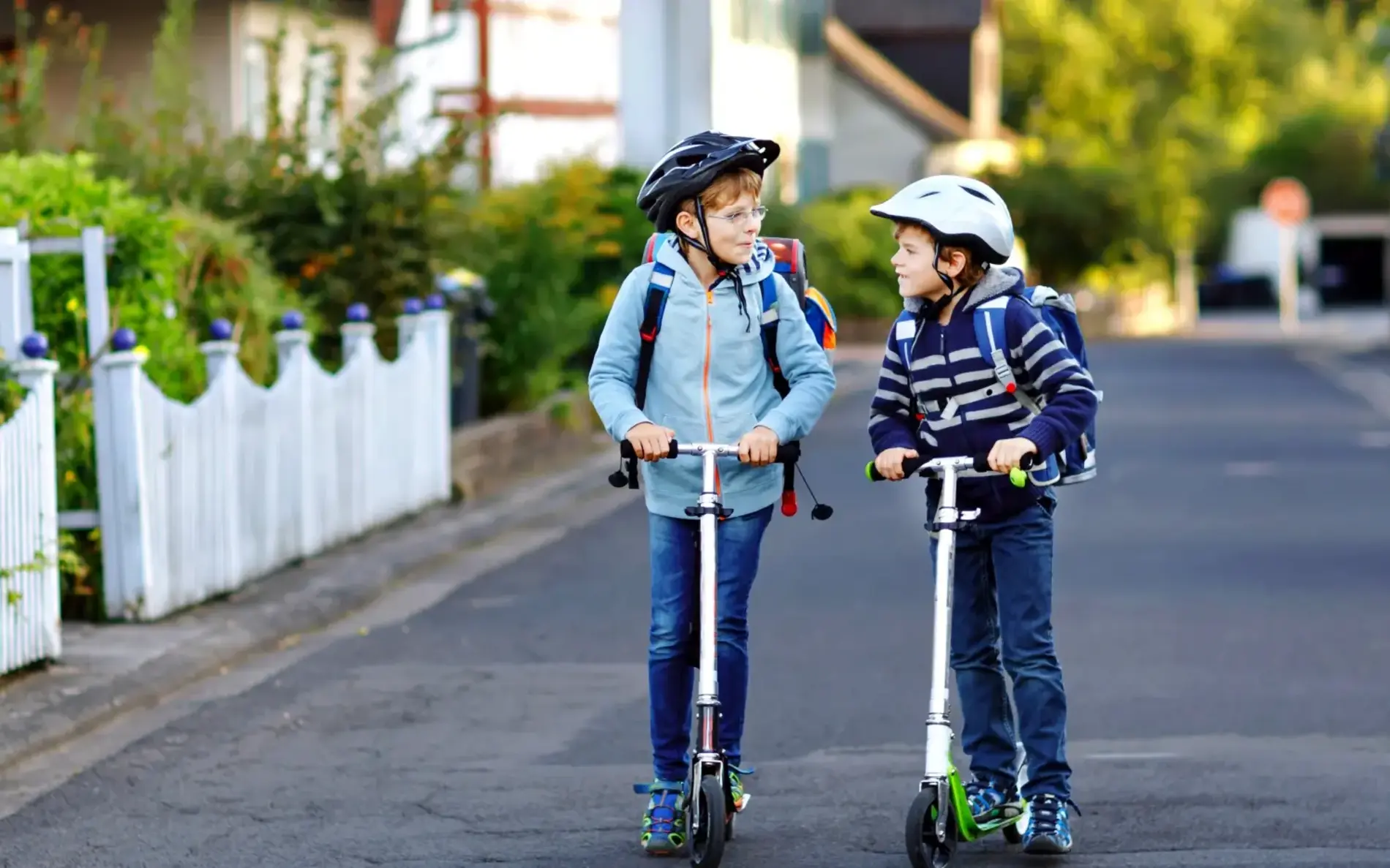 Zwei Kinder auf Tretrollern befahren eine Straße in einer Siedlung
